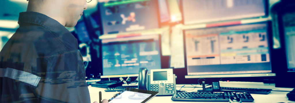 worker with hardhat and tablet in control room with screens