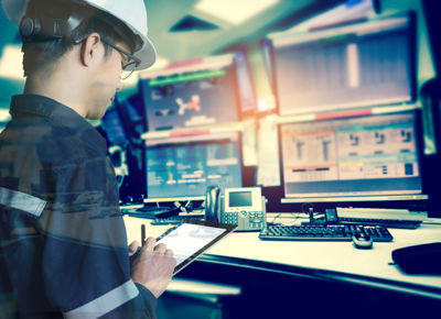 worker with hardhat and tablet in control room with screens